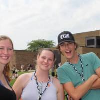 Three students standing outside in summer clothes smiling for a picture